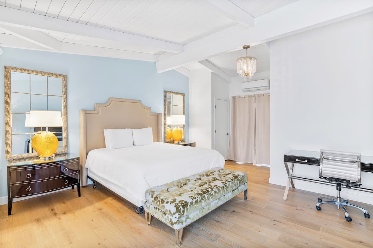 A bedroom with a large bed, bedside lamps, a bench, a desk, and a mirror.