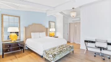 A bedroom with a large bed, bedside lamps, a bench, a desk, and a mirror.