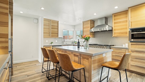 A modern kitchen with wooden cabinets, a large island with bar stools, a stainless steel range hood, and a built-in oven. - Pacific Crest Hotel Santa Barbara (Santa Barbara)