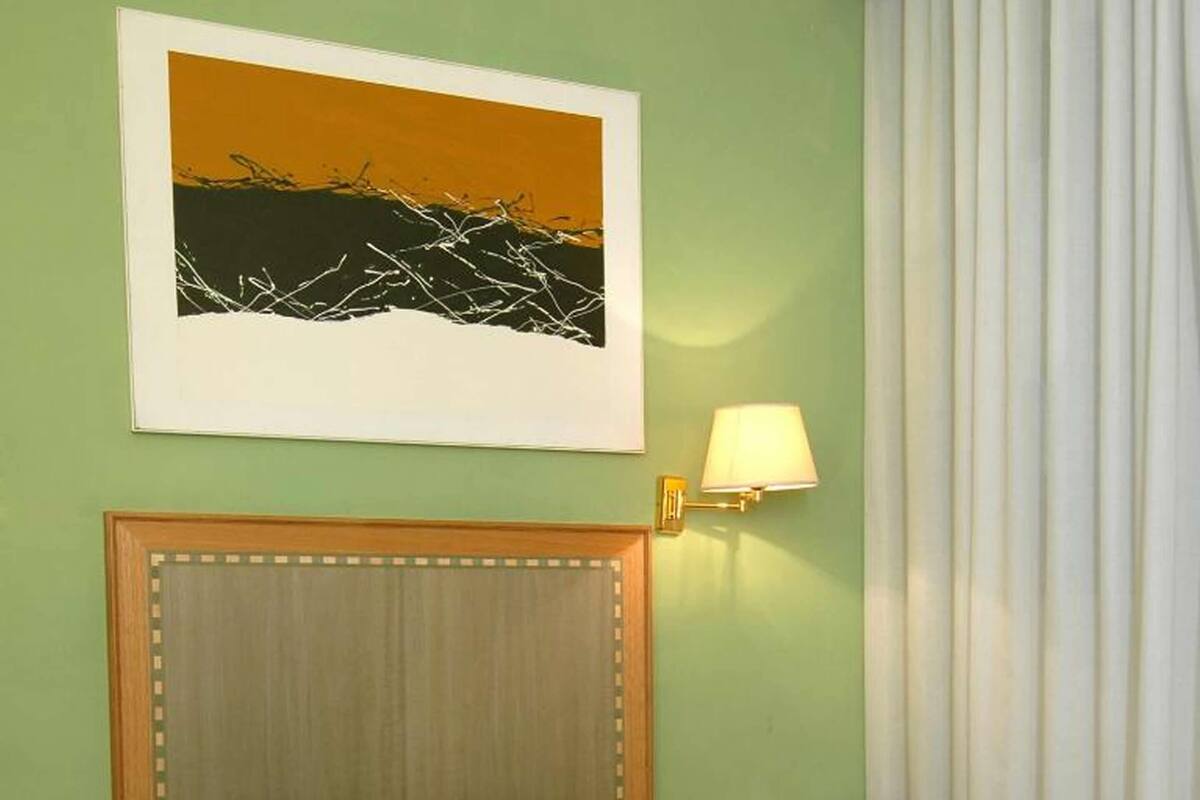 Habitación de hotel con cama, mesita de noche, lámpara y un cuadro en la pared.