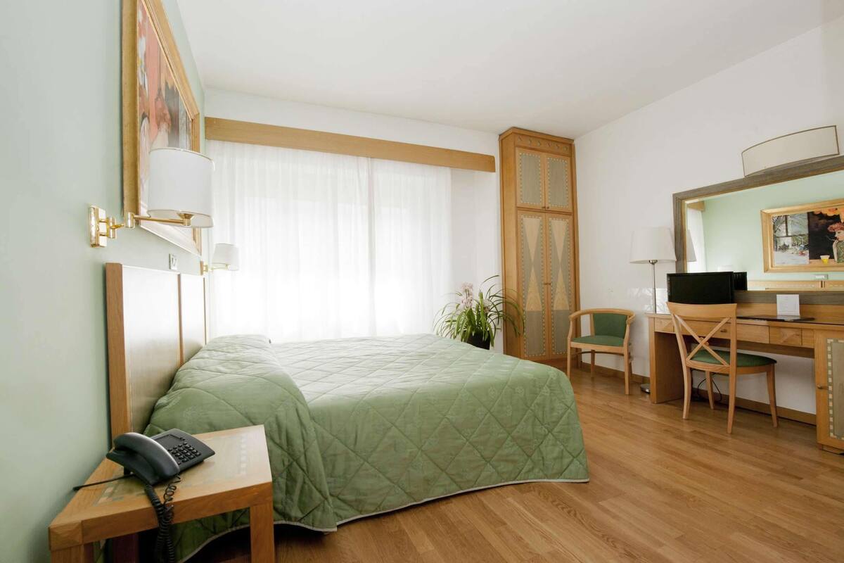 Una habitación de hotel con cama, escritorio, silla y espejo.