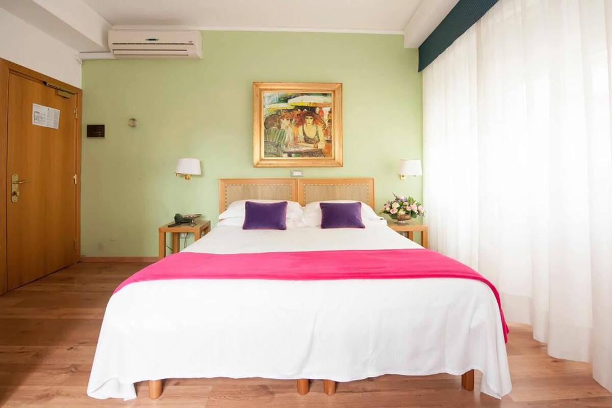 Una habitación de hotel con una cama, una mesita de noche, un cuadro y una puerta.