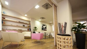 A modern interior with a reception desk, seating area, and a bookshelf. - Hotel Touring Pisa (Pisa)