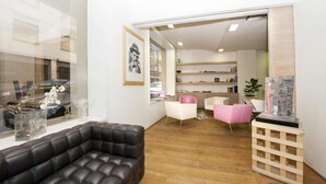 A modern living room with a leather sofa, white chairs, a wooden coffee table, and a glass display case with flowers. - Hotel Touring Pisa (Pisa)