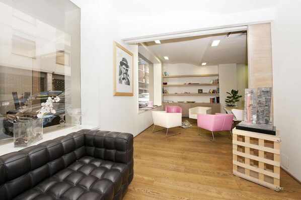 A modern living room with a leather sofa, white chairs, a wooden coffee table, and a glass display case with flowers.