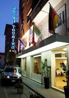 A hotel with a sign reading "HOTEL TOURING" and multiple flags displayed outside.