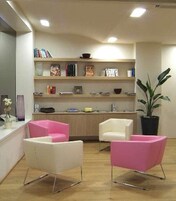A modern living room with two pink chairs, a white chair, and a bookshelf filled with books and decorative items.