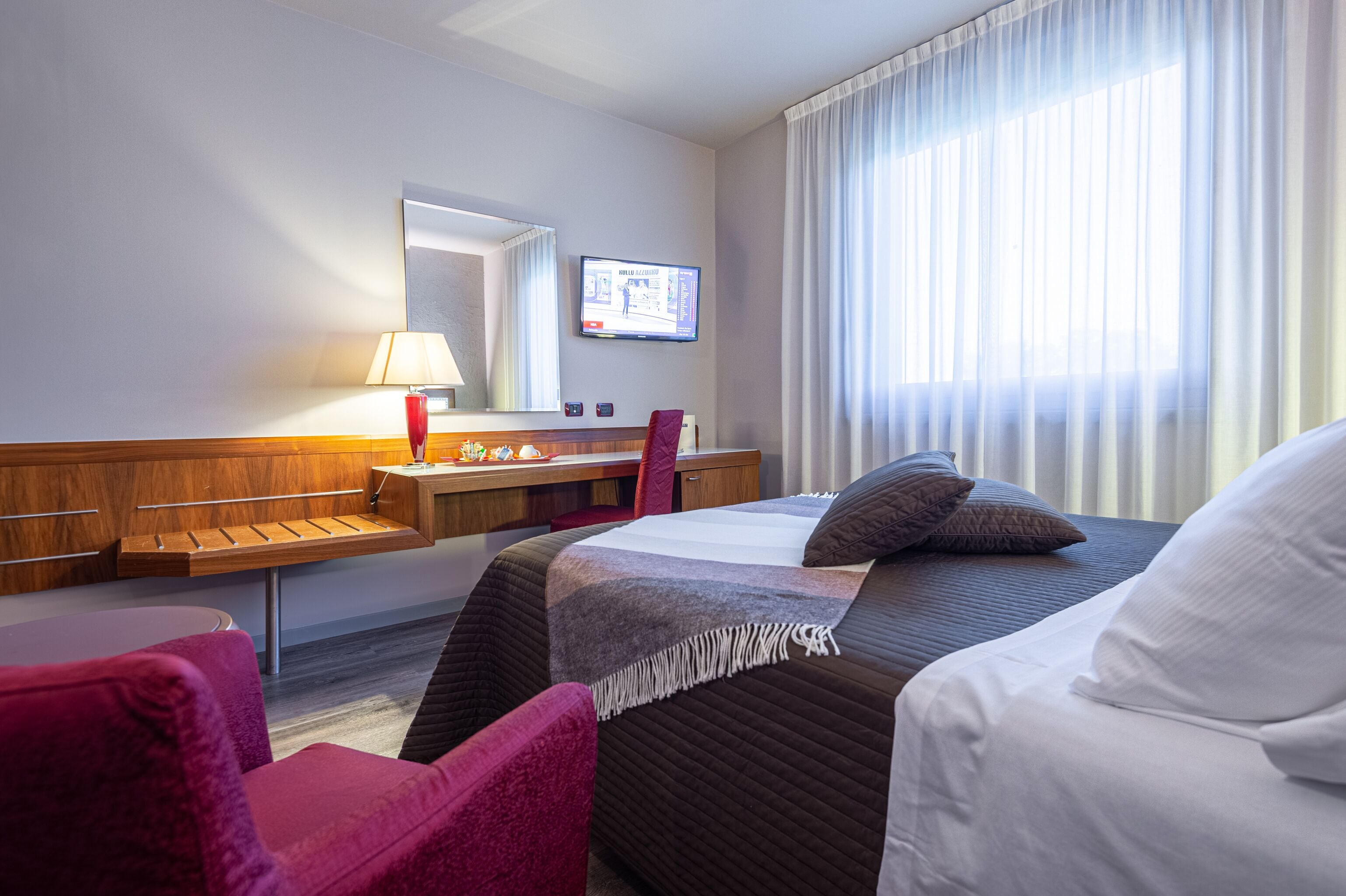 A hotel room with a bed, a desk, a chair, a television, and a window with curtains.