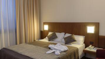 A hotel room with a neatly made bed, a bedside table with a phone and a lamp, and a red chair.