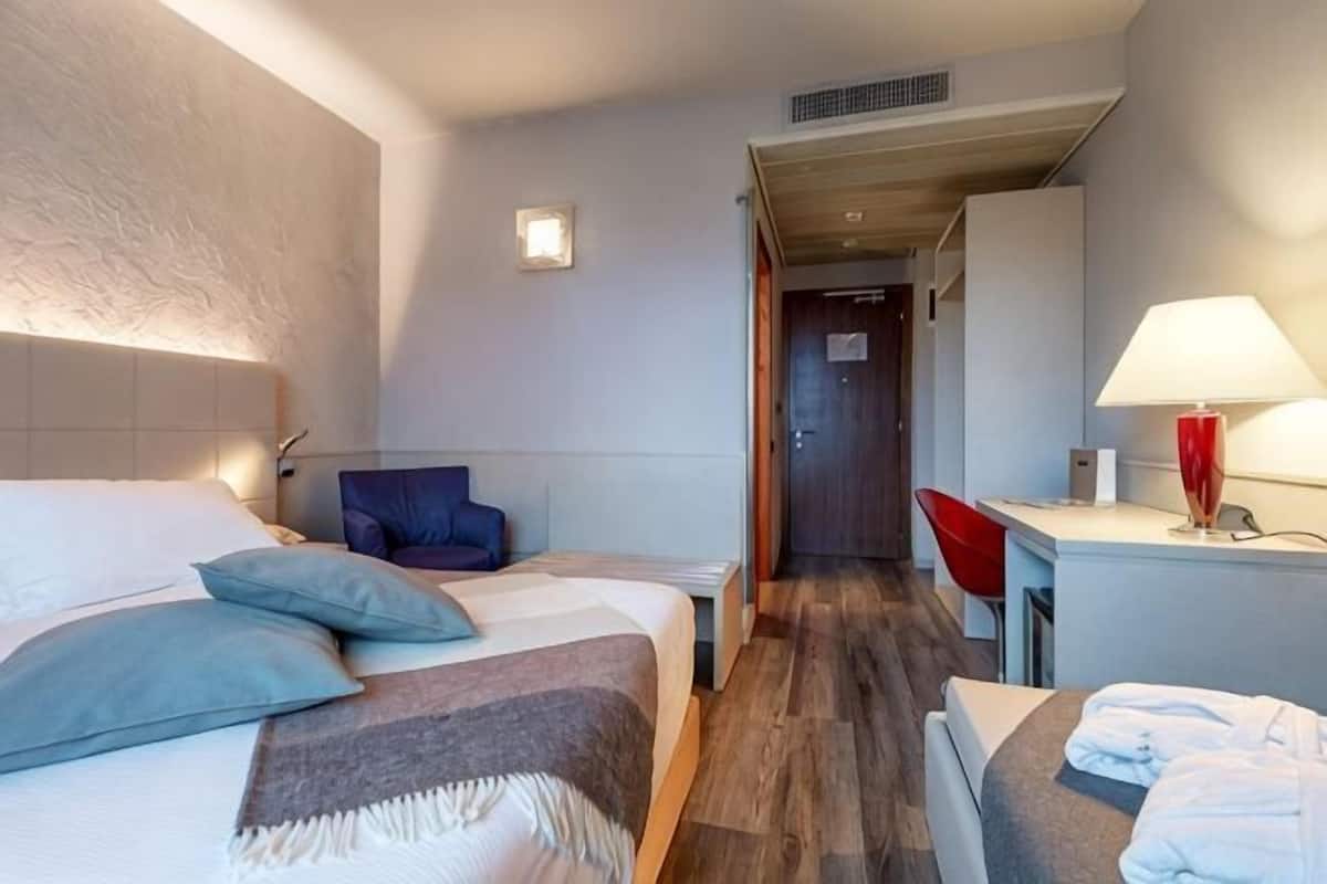 A hotel room with a bed, bedside table, lamp, chair, and a desk with a chair.