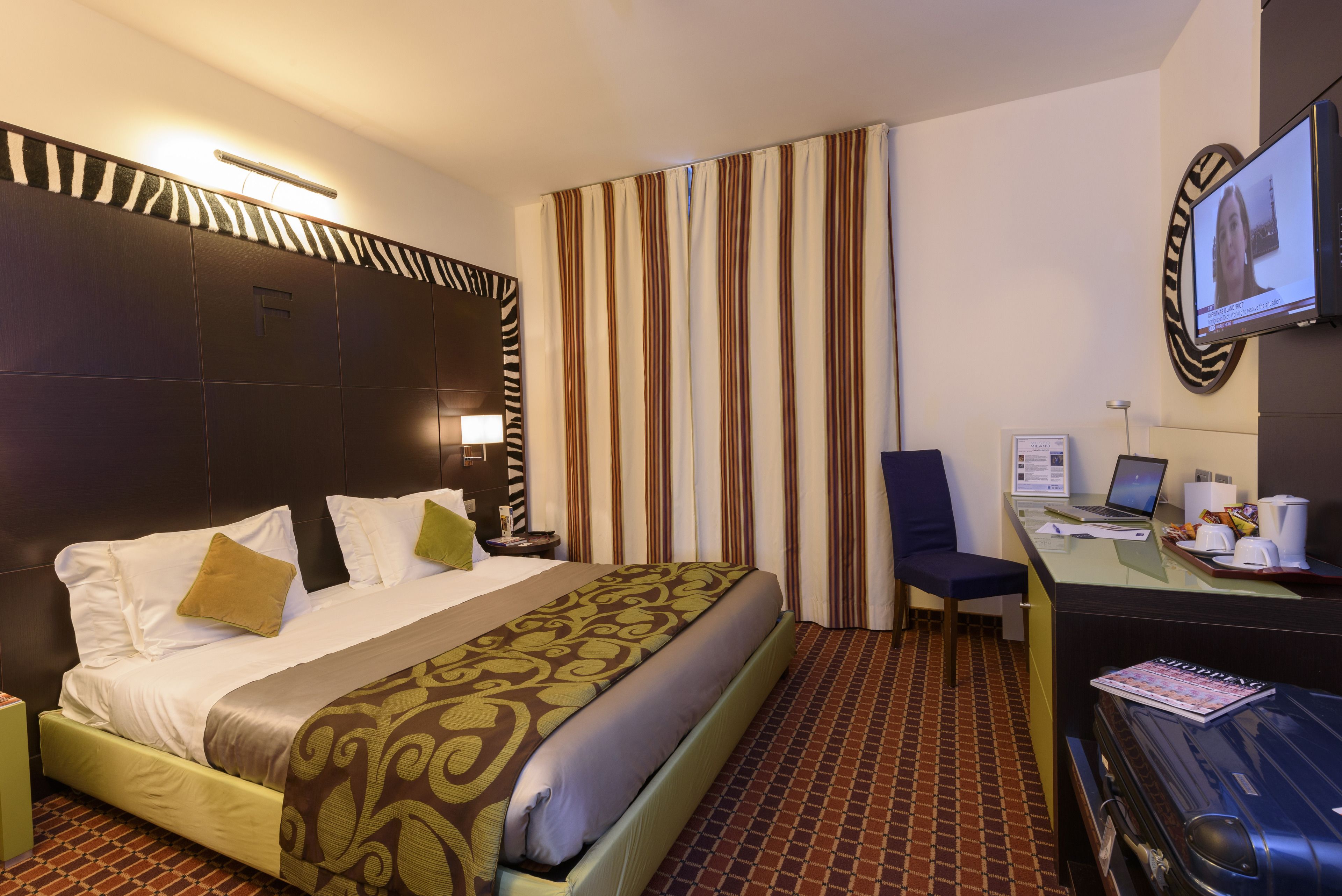 A hotel room with a large bed, a desk with a laptop, a television, and a suitcase.