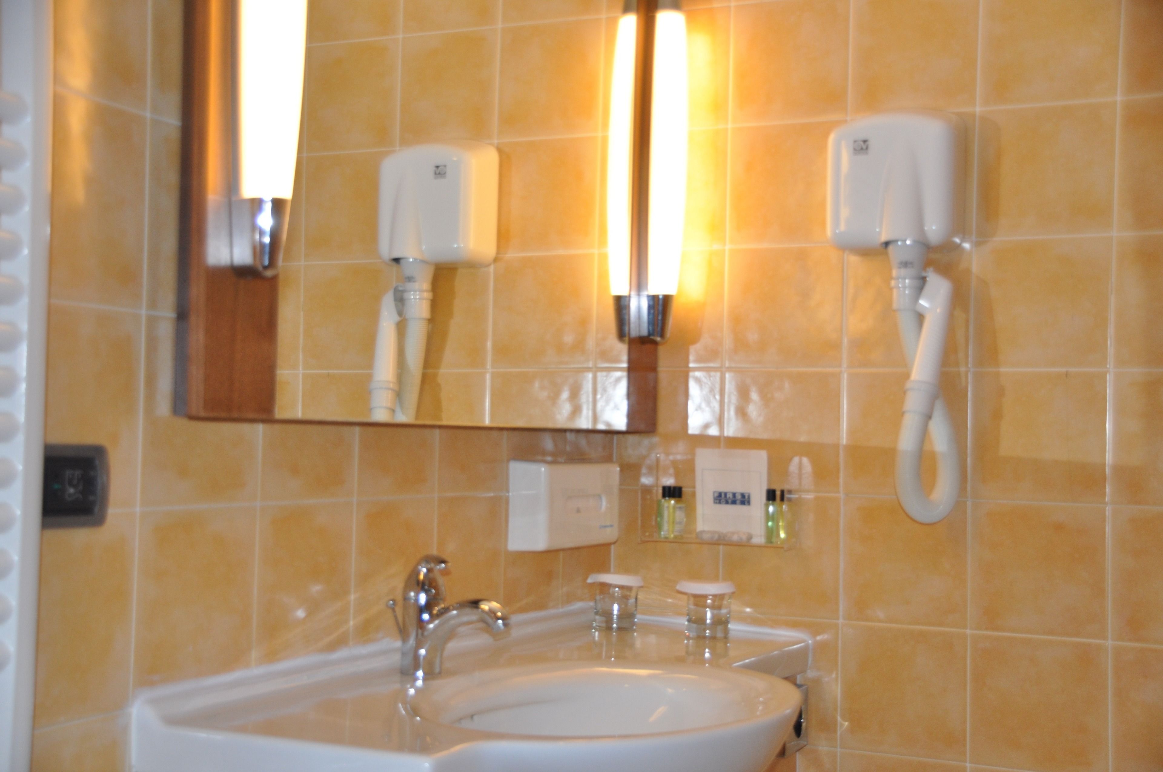 Un baño con lavamanos, espejo y dos secadores de manos fijos a la pared.