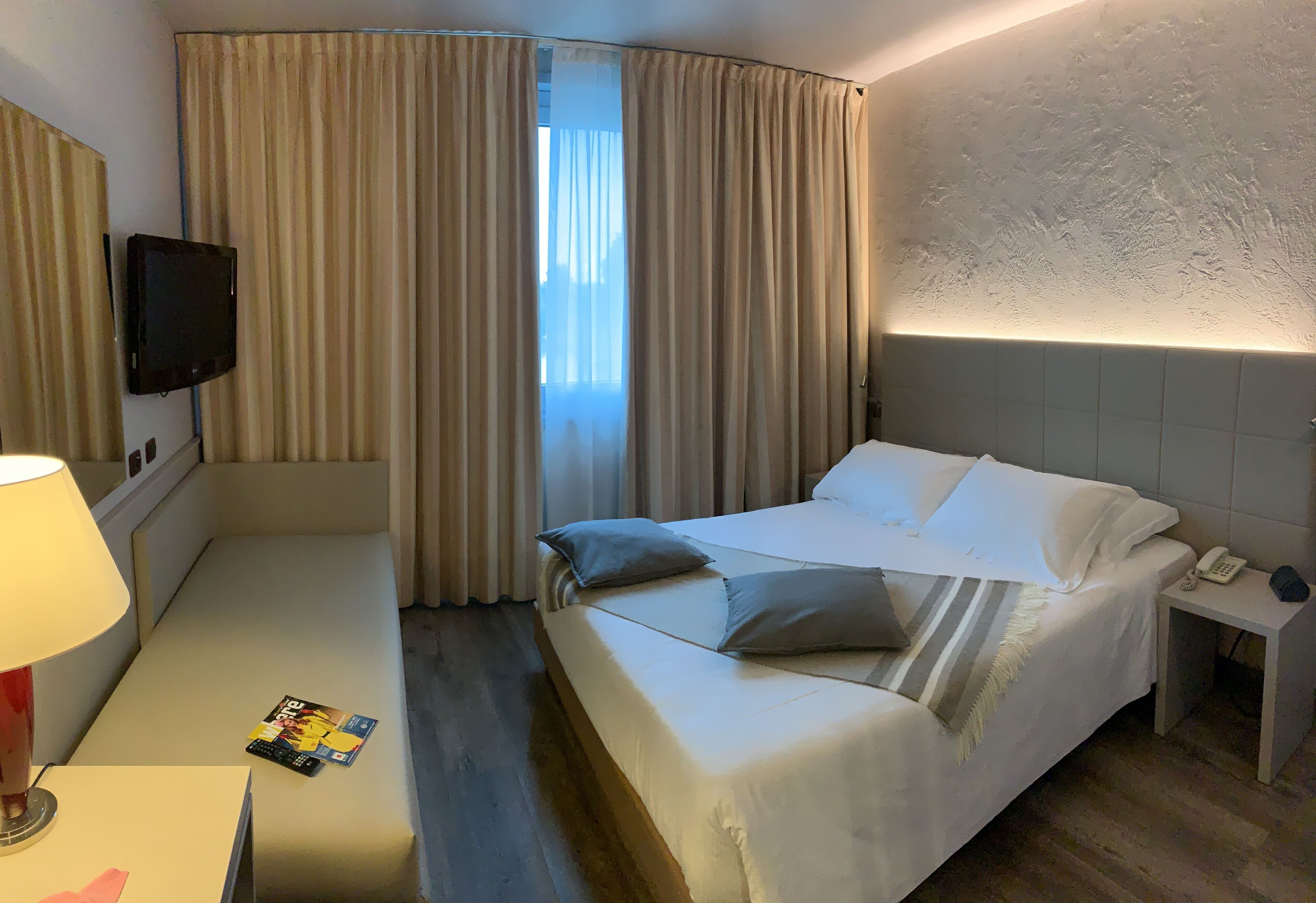 A hotel room with a bed, bedside table, lamp, and curtains.