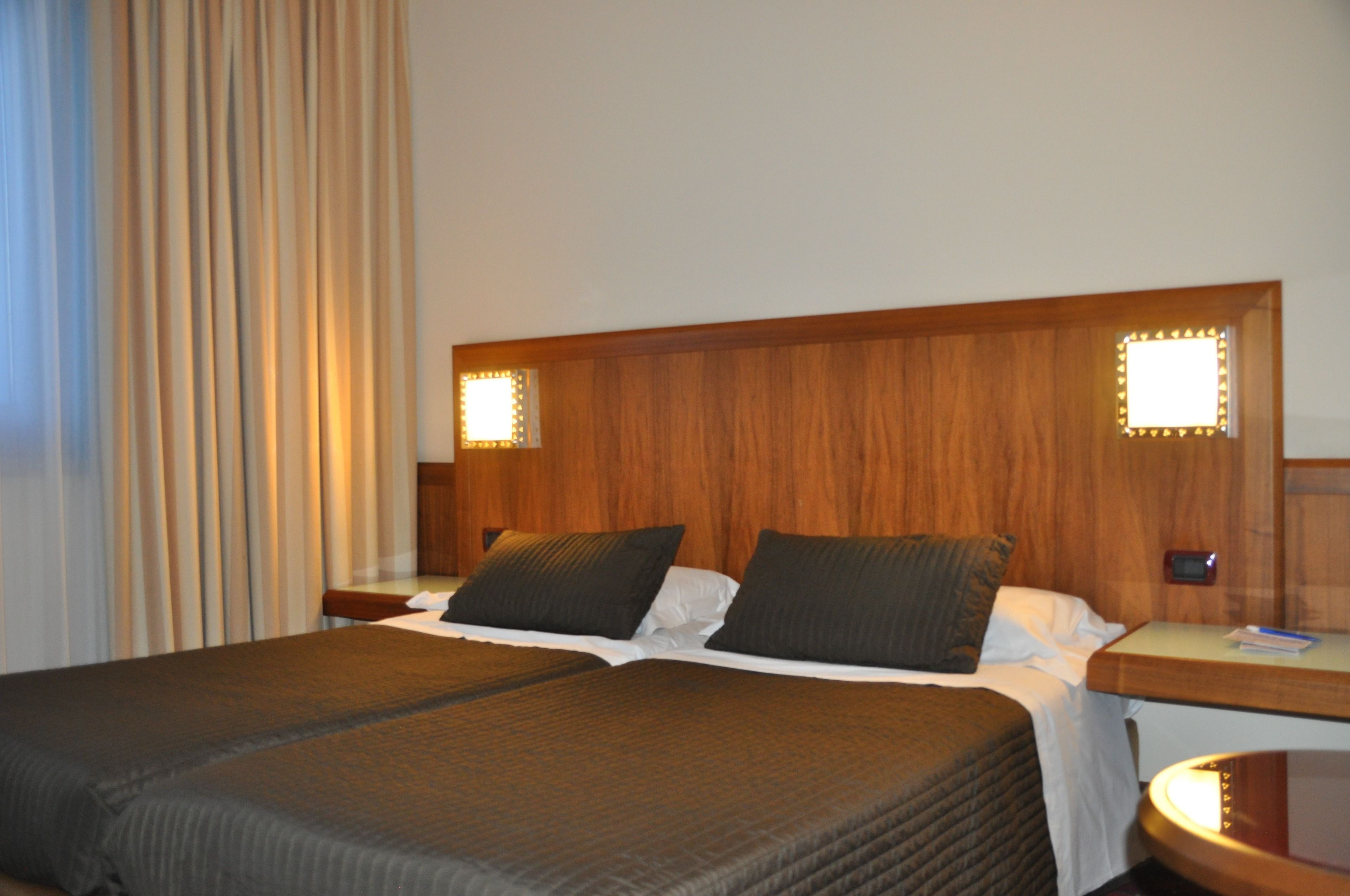 A hotel room with a large bed, wooden headboard, two bedside tables, and a nightstand.