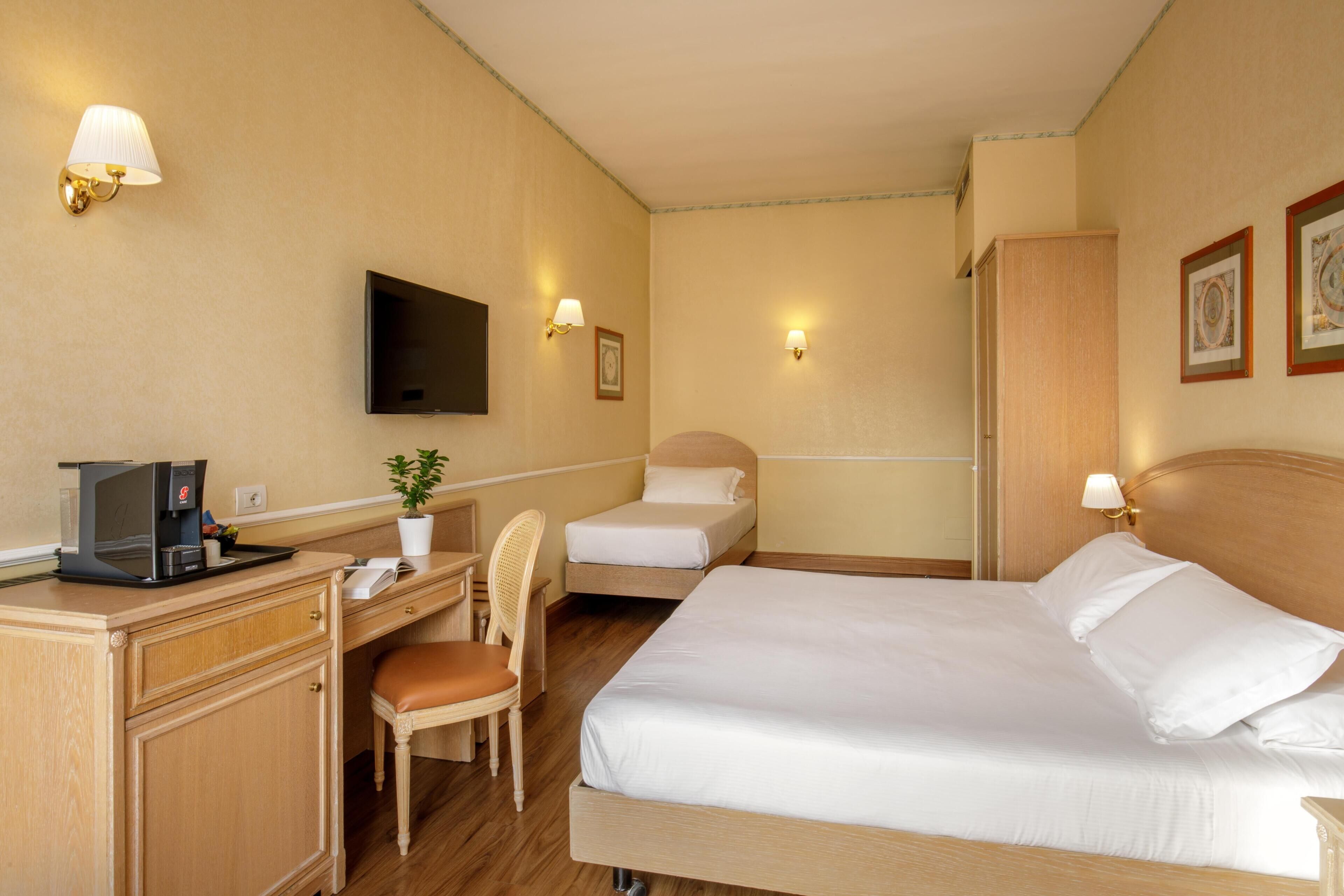 A hotel room with a bed, desk, chair, television, and wall-mounted lamps.