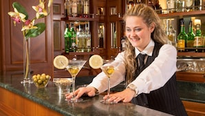 Zona de bar con un bartender, dos copas de martini con rodajas de limón, un jarrón con flores y un cuenco de aceitunas.