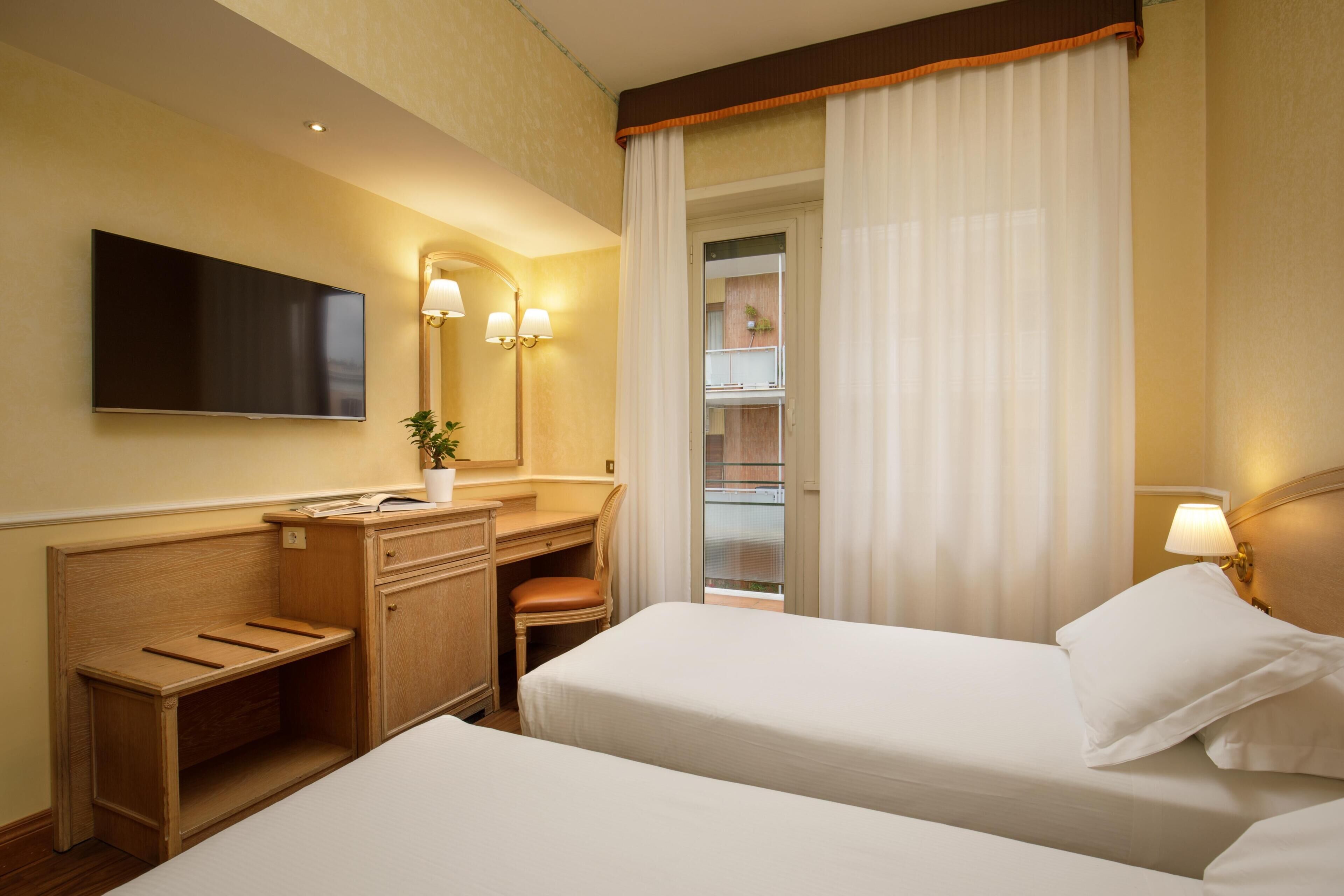 A hotel room with a bed, a desk, a chair, a TV, and a bathroom mirror.
