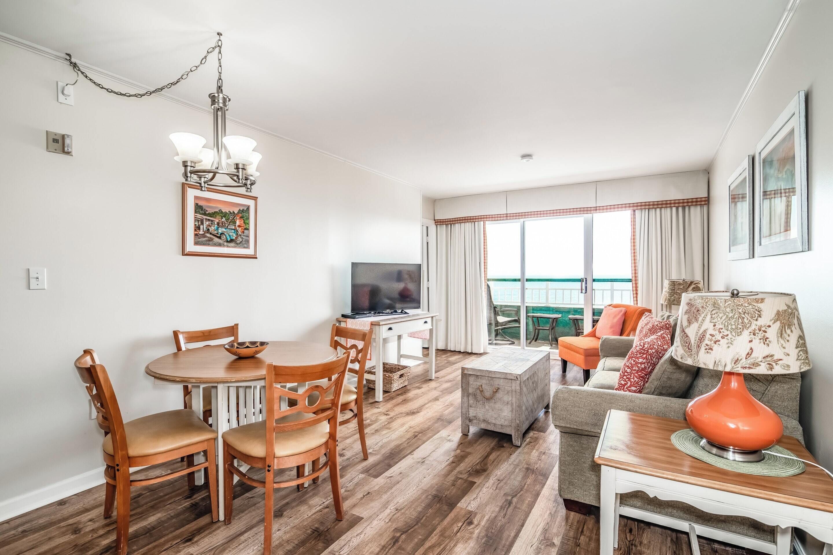 Een woonkamer met een eettafel, stoelen, een televisie, een bank en een lamp.