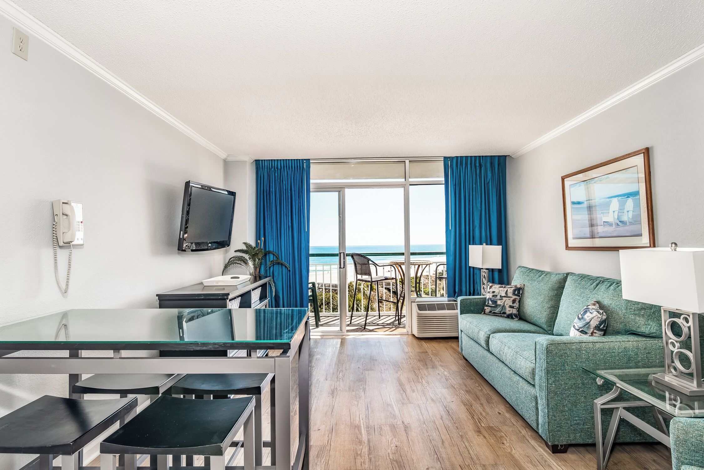 Habitación de hotel con balcón, sofá, televisor, escritorio y una silla.