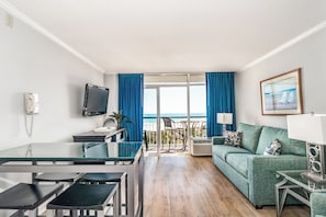 A hotel room with a balcony, a sofa, a TV, a desk, and a chair. - Litchfield Beach & Golf Resort (Pawleys Island)