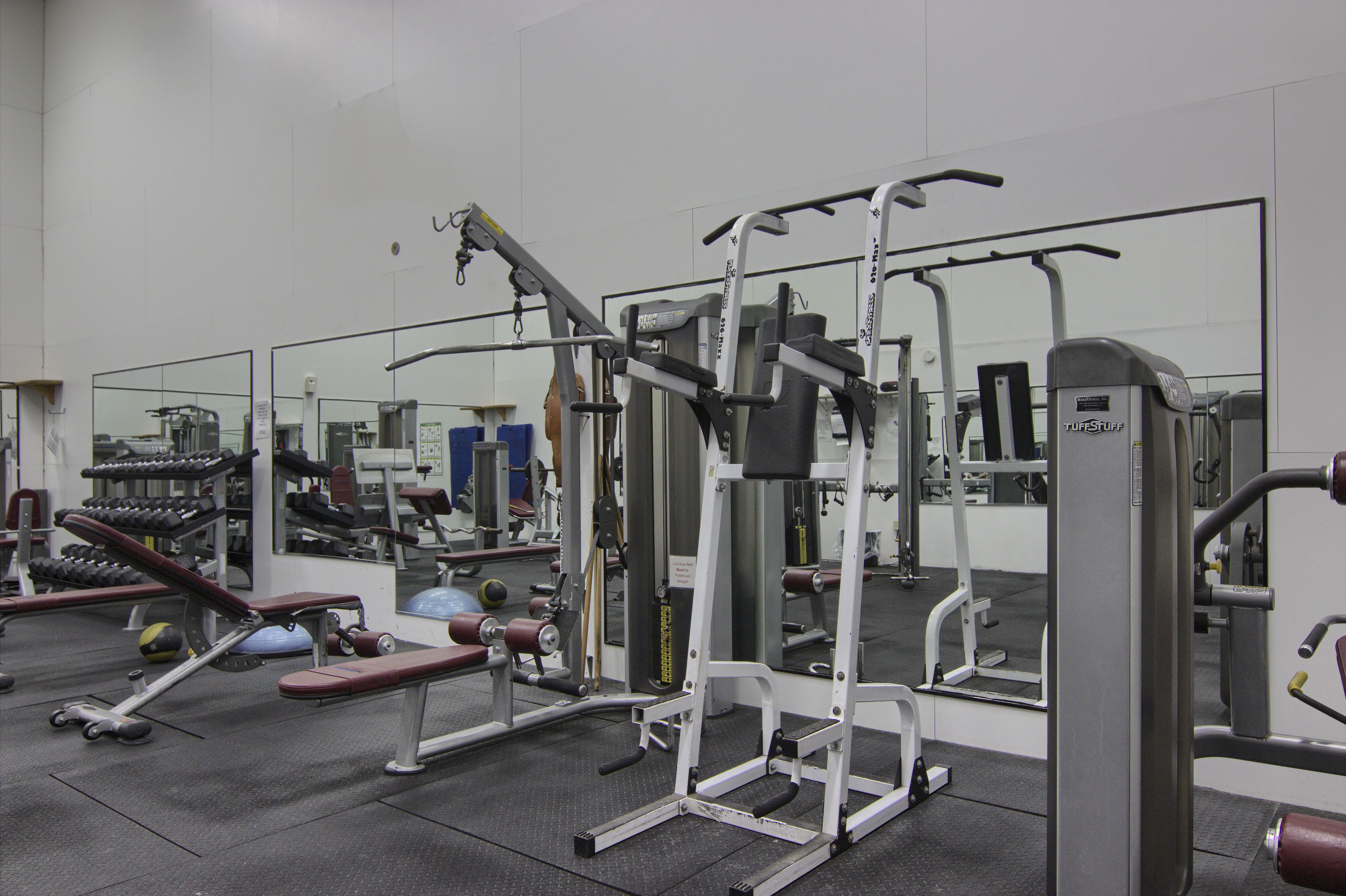 Une salle de sport équipée de divers appareils d’exercice, notamment des bancs, des machines de musculation et un mur recouvert de miroirs.