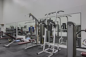 Ein Fitnessstudio mit unterschiedlicher Trainingsausstattung, darunter Bänke, Kraftgeräte und eine Spiegelwand.