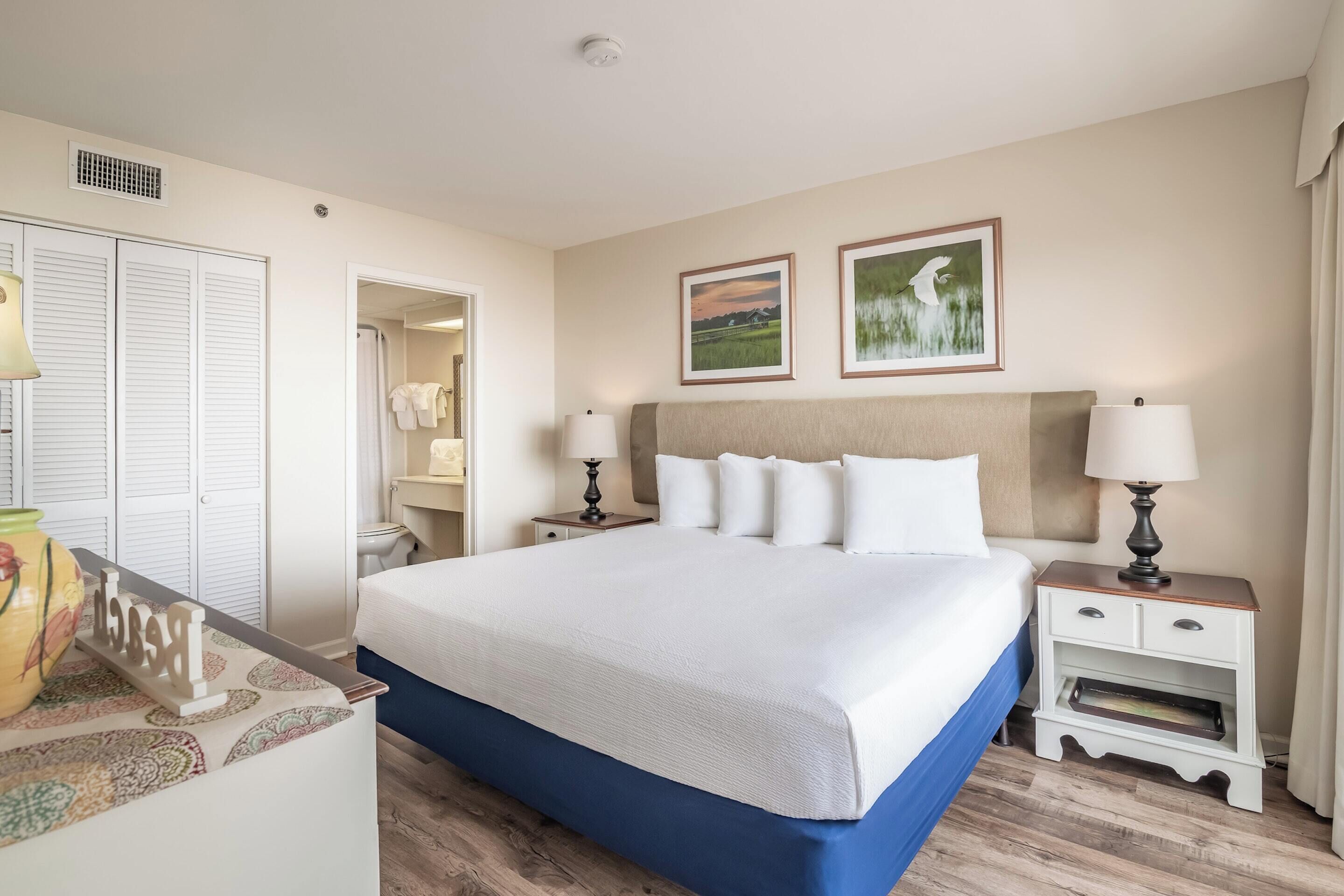 Quarto de hotel com uma cama, mesas de cabeceira, um guarda-roupa e um banheiro visível por uma porta aberta.