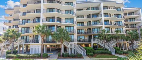 A multi-story hotel with balconies, a swimming pool, and palm trees.