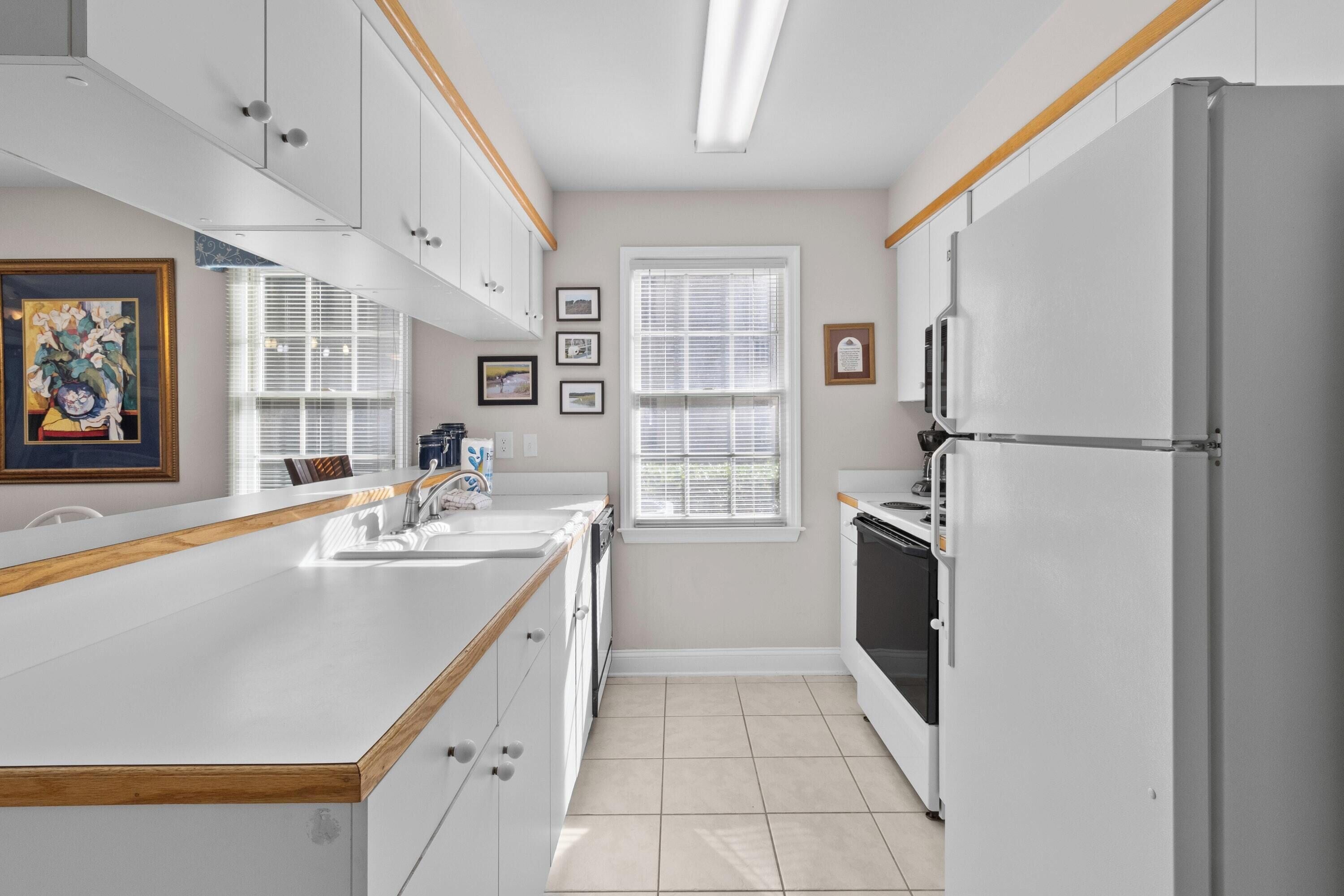 A modern kitchen with white cabinetry, a wooden countertop, a refrigerator, and a window with blinds.