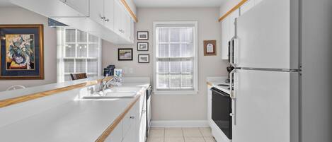 A modern kitchen with white cabinetry, a wooden countertop, a refrigerator, and a window with blinds.