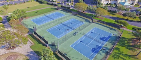 Un hotel de varios pisos con un complejo de canchas de tenis.