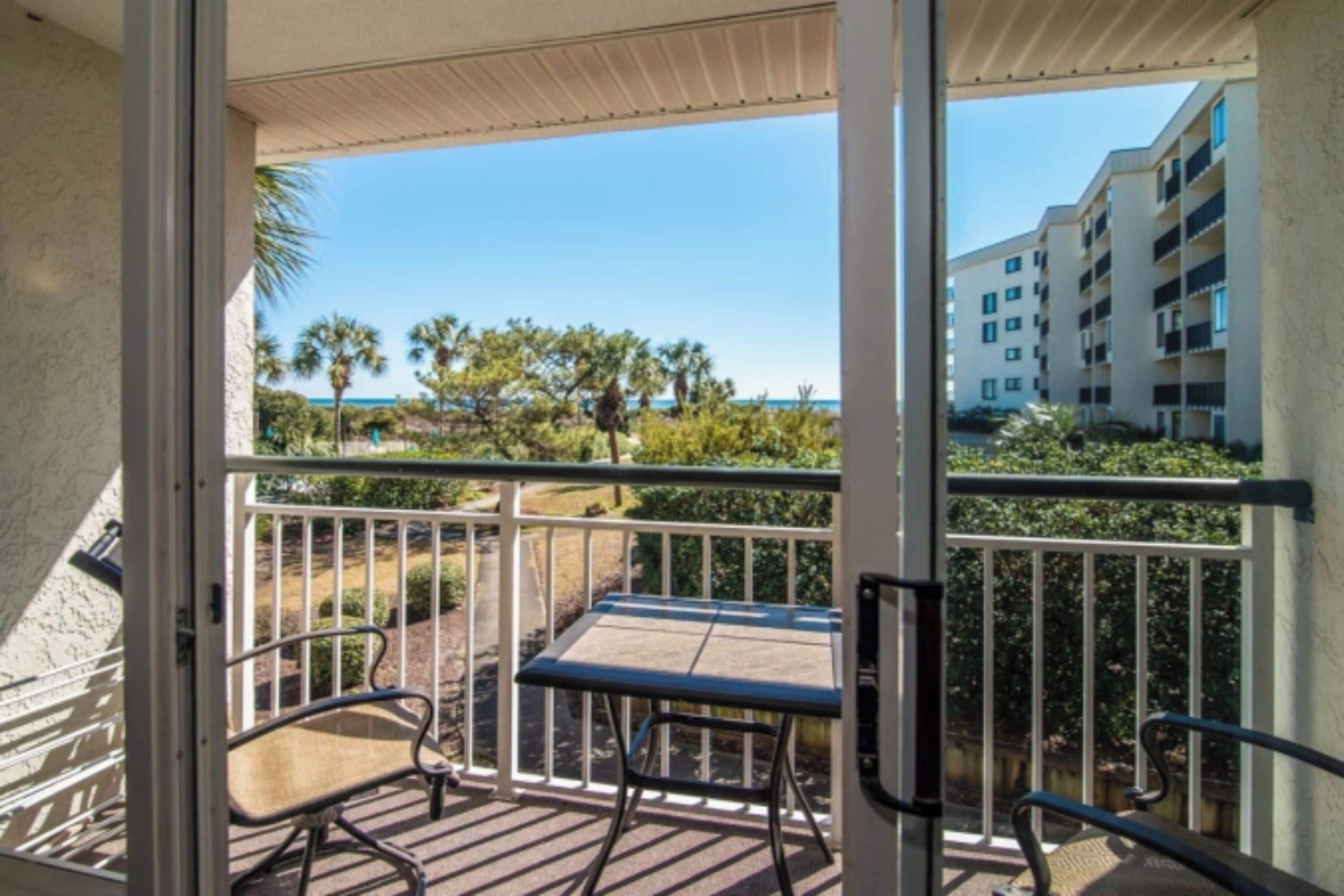 A balcony with a table and chairs, overlooking a beach and a building.