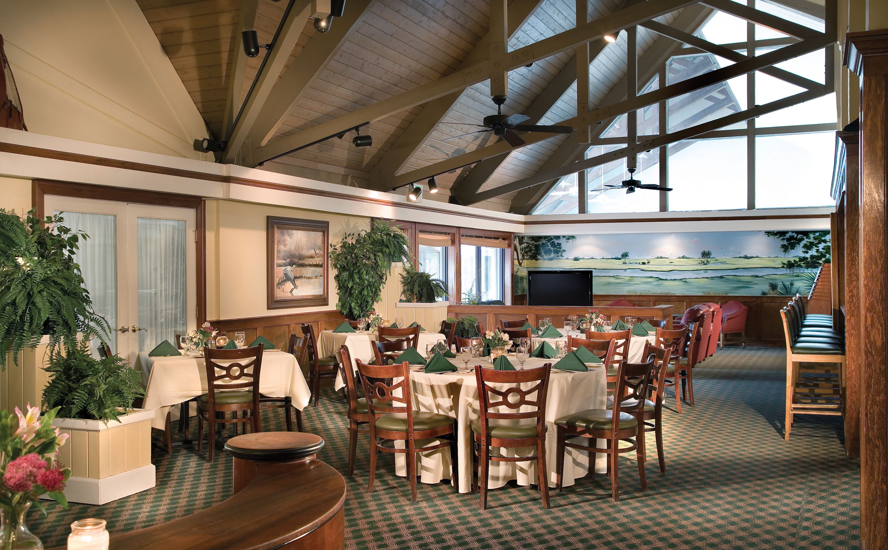 A dining area with tables set for a meal, wooden chairs, and a large window with a view of a landscape.