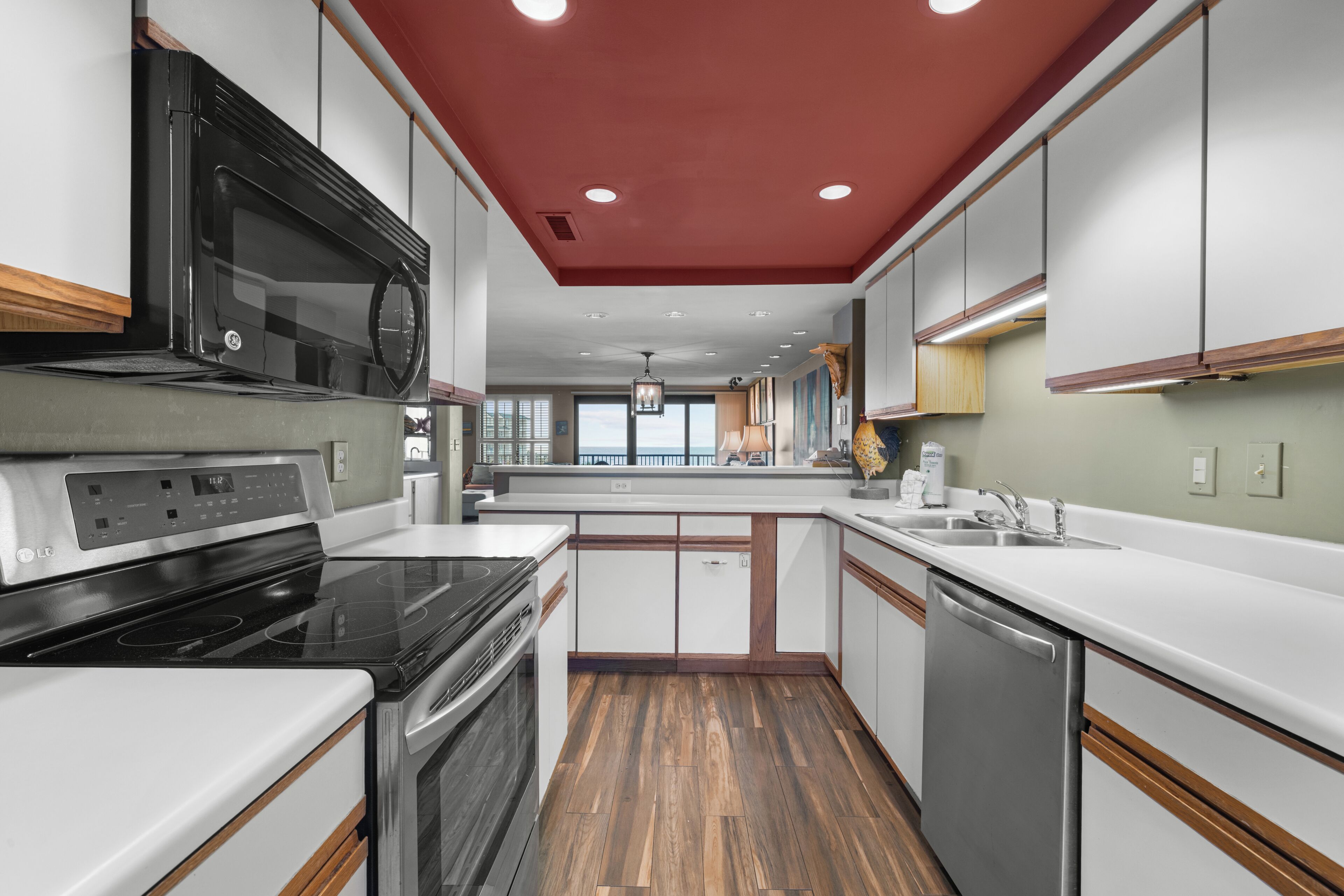 A modern kitchen with a red ceiling, stainless steel appliances, and wooden flooring.