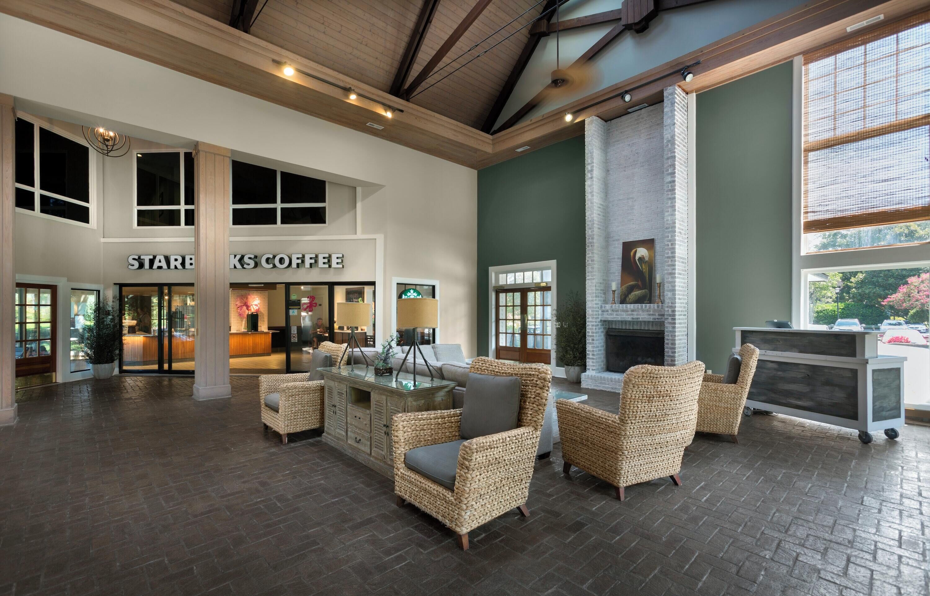 Un amplio vestíbulo con el letrero de Starbucks Coffee, muebles de mimbre, chimenea y ventanas grandes.