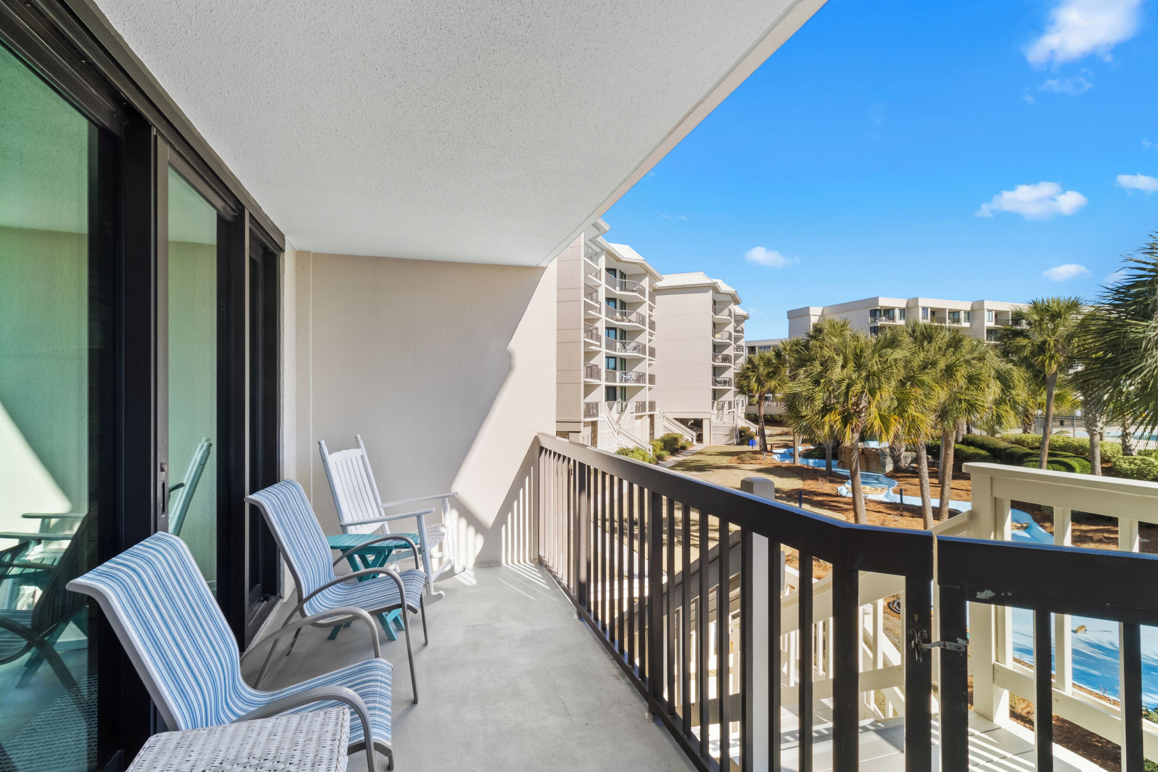 A balcony with wicker chairs, a pool, and a view of a resort building.