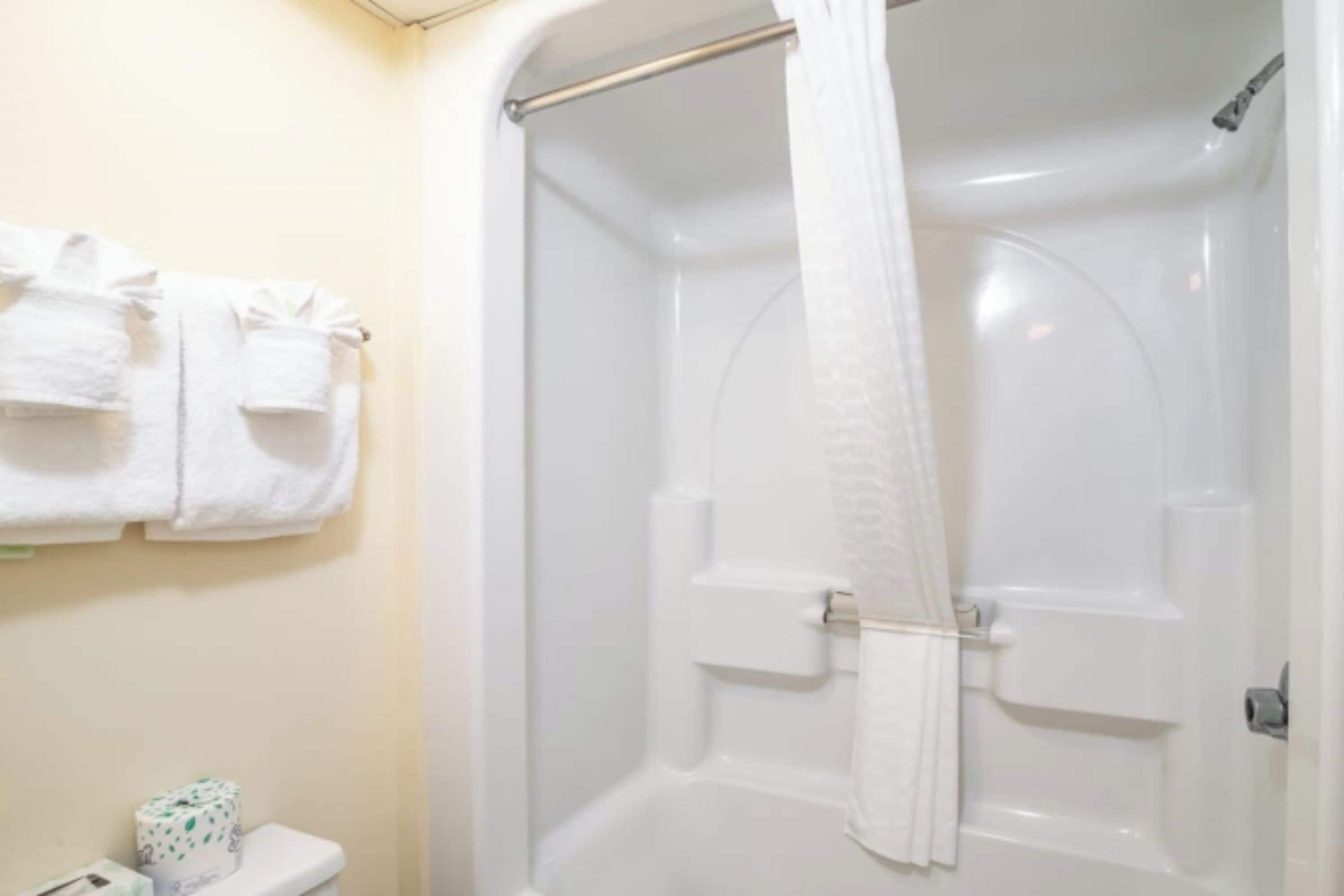 A bathroom with a shower, a toilet, and a towel rack with towels.