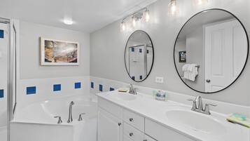 A modern bathroom with a bathtub, two sinks, a large mirror, and a framed picture on the wall.