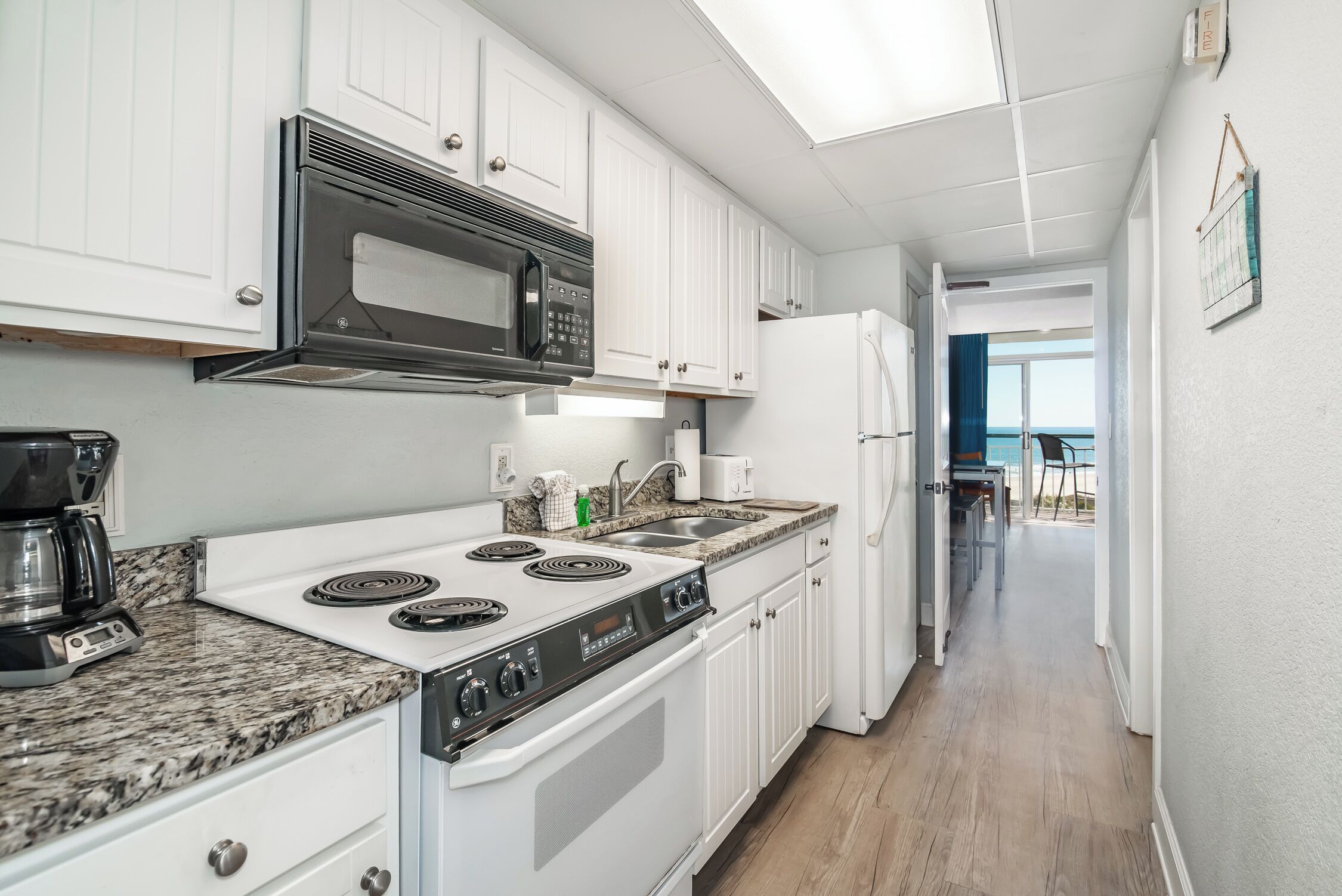 A modern kitchen with white cabinetry, a black microwave, a stove, and a refrigerator.