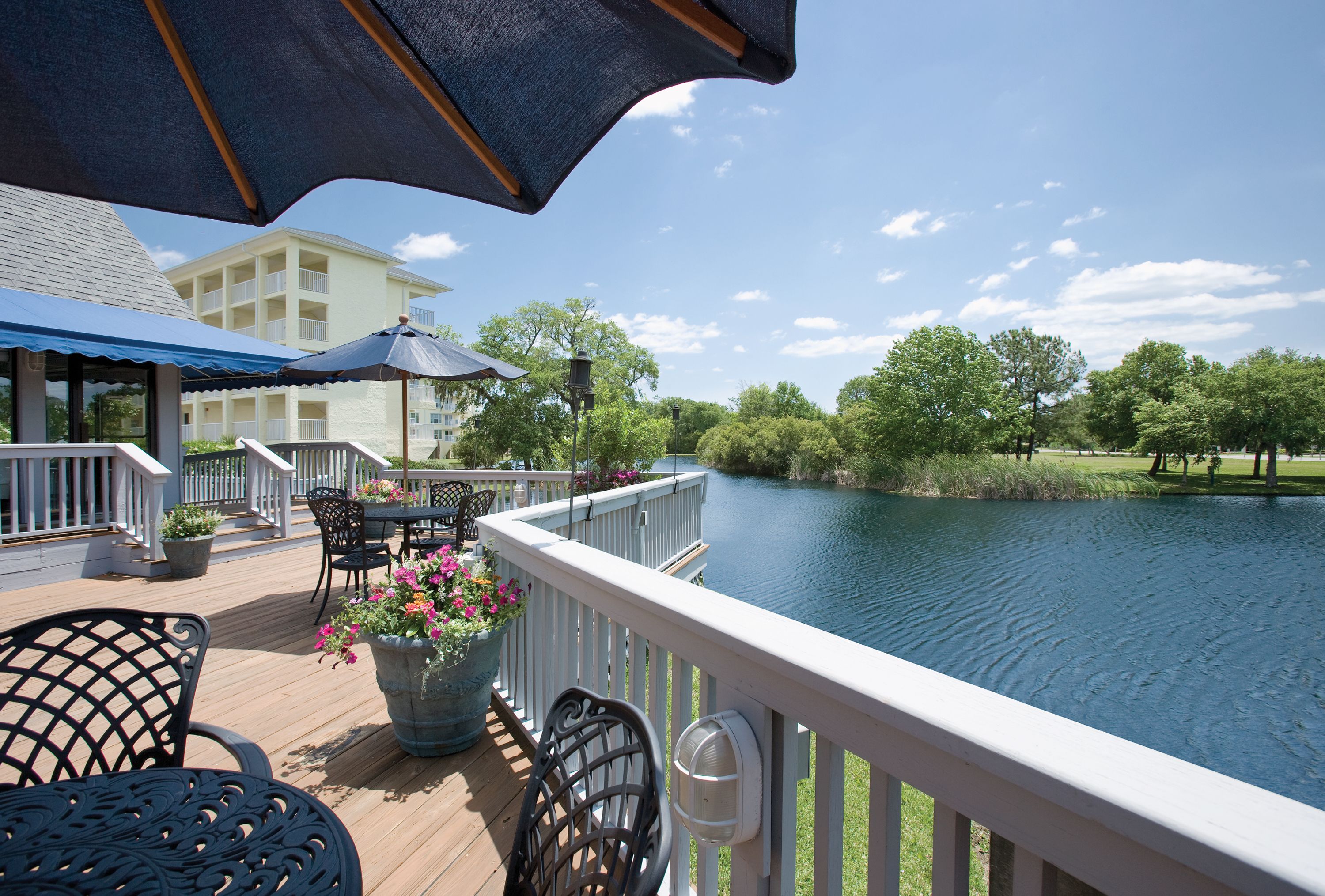 A deck with outdoor seating, a view of a lake, and a building in the background.