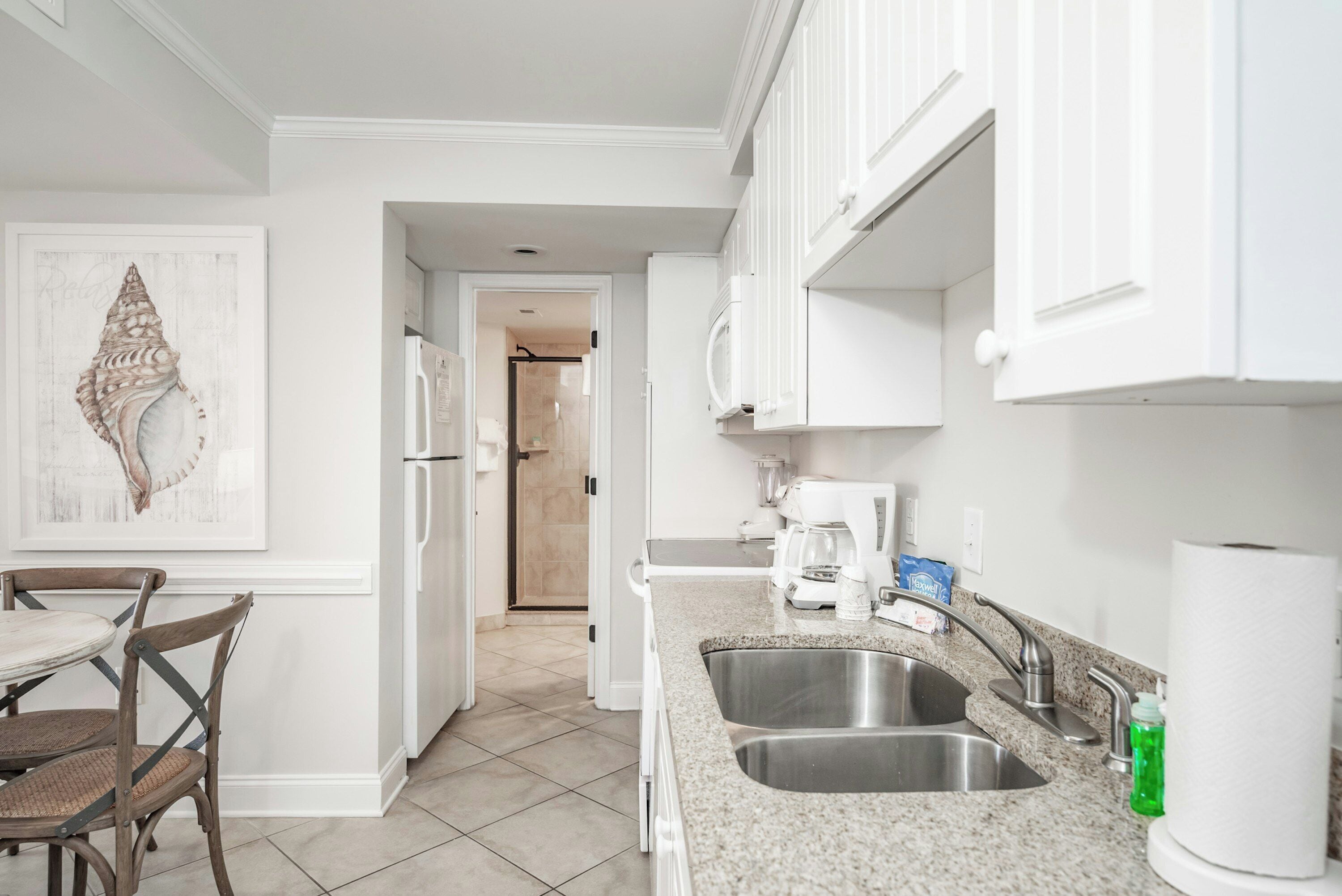 A modern kitchen with white cabinets, a granite countertop, a stainless steel sink, and a dining area with a table and chairs.