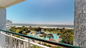 A view of a beach resort with a pool area, palm trees, and a building in the background. - Litchfield Beach & Golf Resort (Pawleys Island)