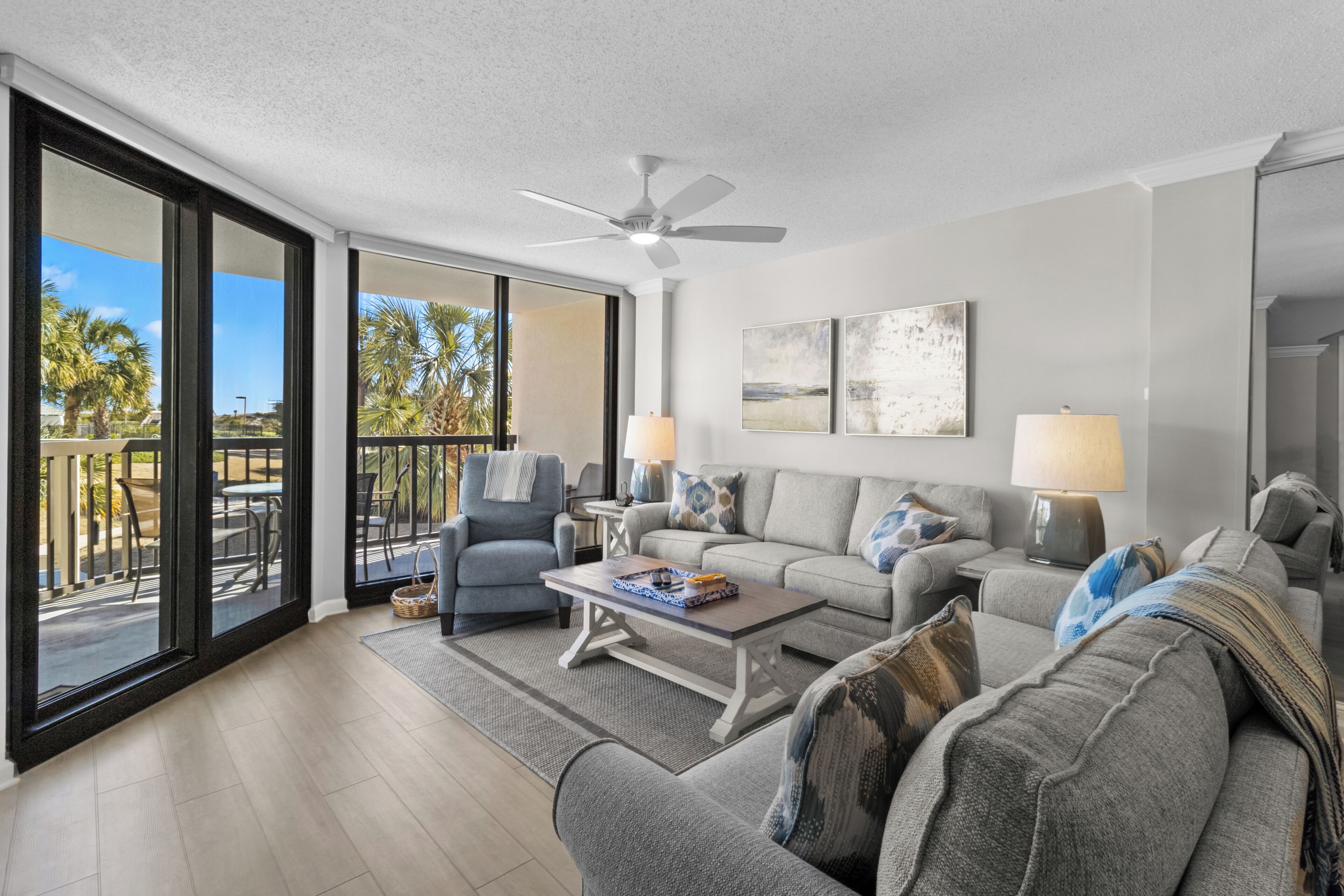 A spacious living room with a large window, a ceiling fan, and a balcony with outdoor furniture.