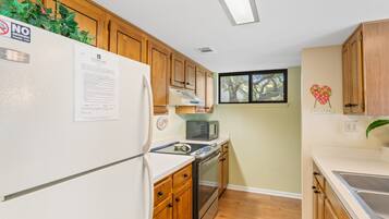 A compact kitchen with wooden cabinets, a white refrigerator, a microwave, and a stove.