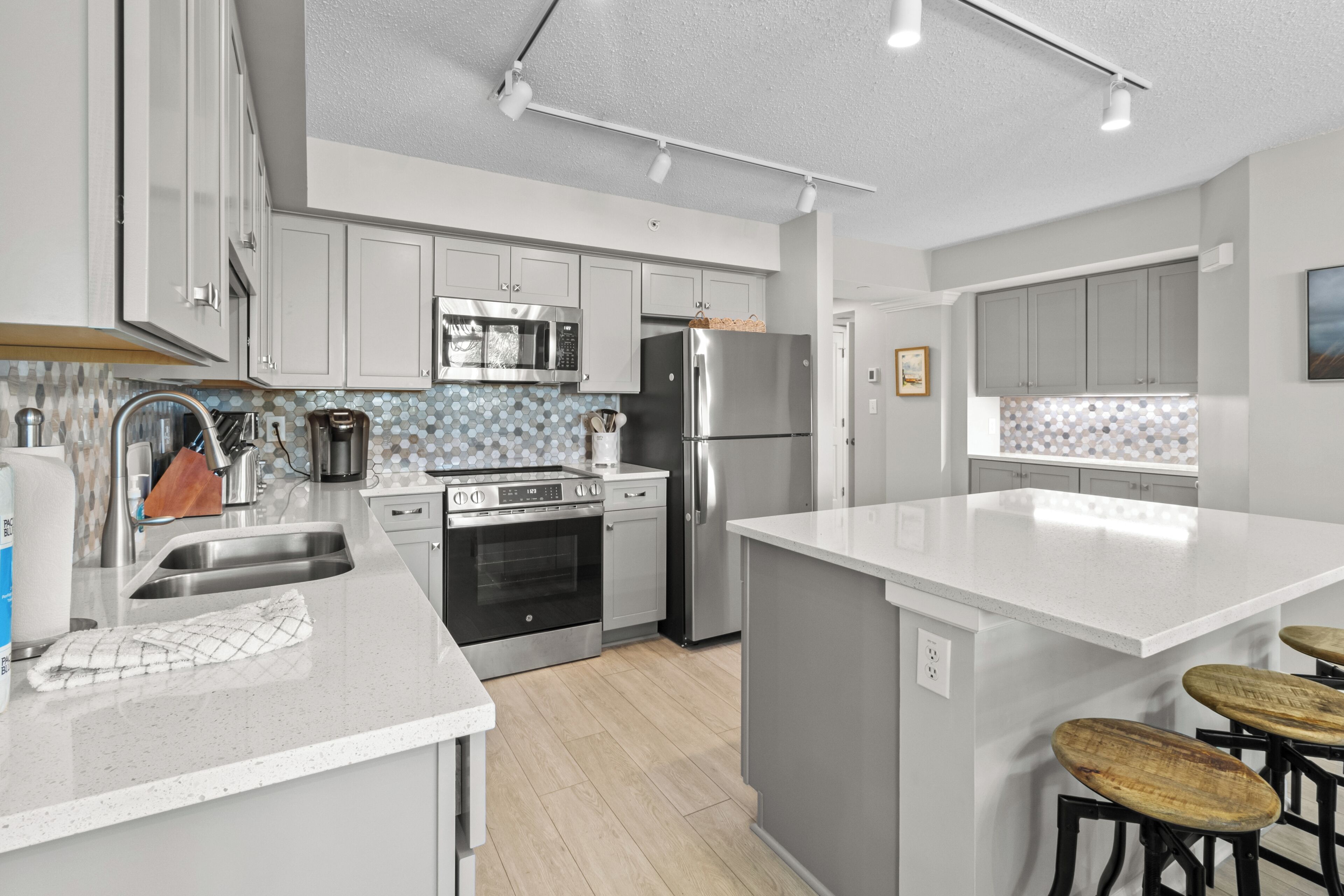 Una cocina moderna con electrodomésticos de acero inoxidable, una isla grande con taburetes altos y un salpicadero de azulejos hexagonales.