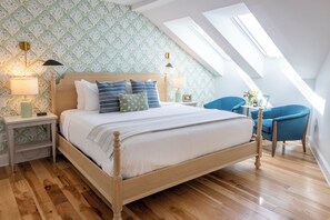 A bedroom with a wooden bed, two nightstands, a blue chair, and a skylight.