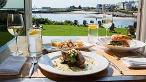 Ein Tisch mit einer Mahlzeit, zwei Gläsern Weißwein und Blick auf Strand und Häuser.