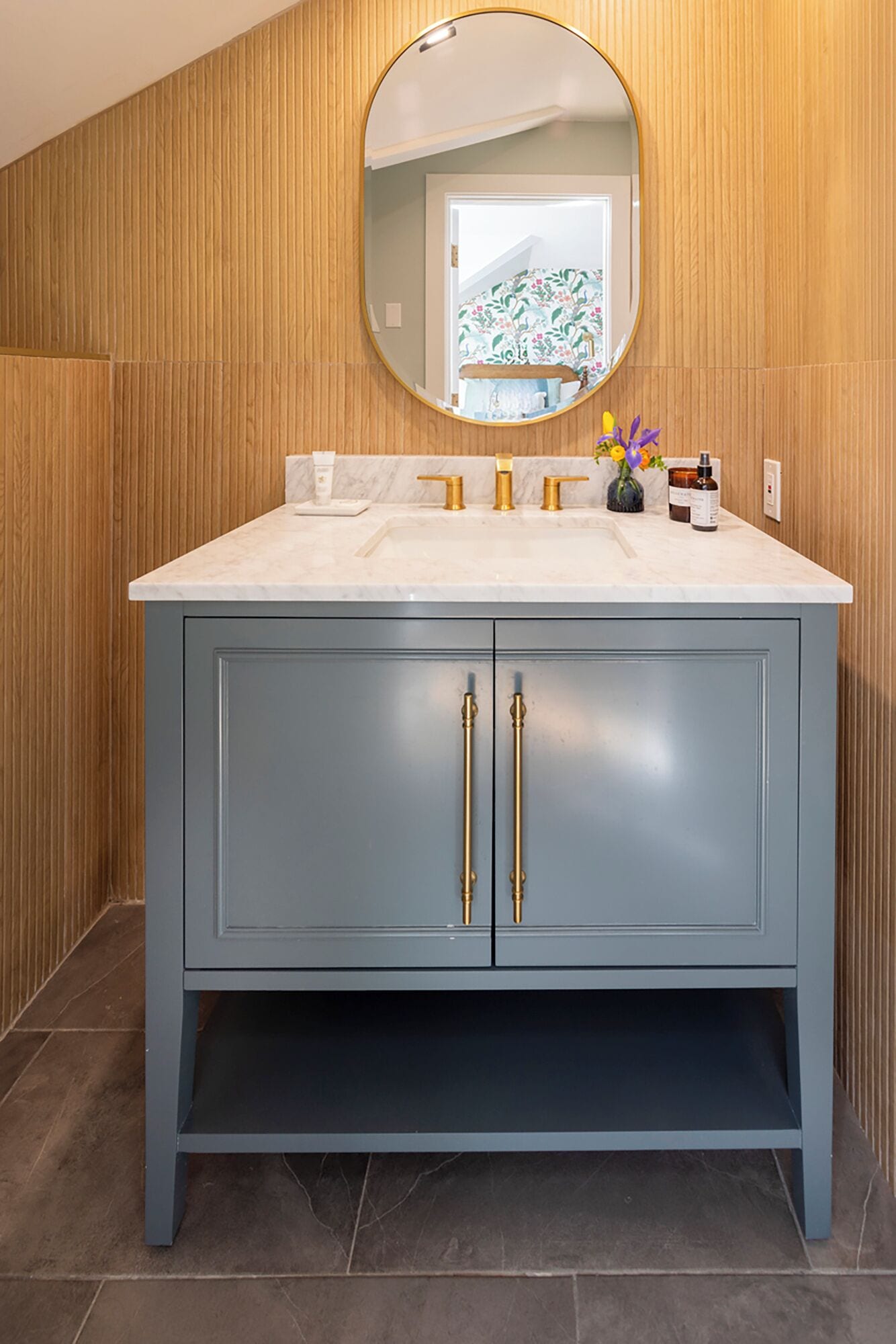 A bathroom with a marble sink, gold faucets, and a blue vanity with gold handles.