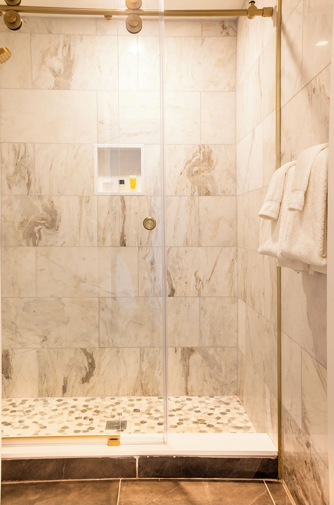 A walk-in shower with a glass door, marble tiles, and a towel rack.