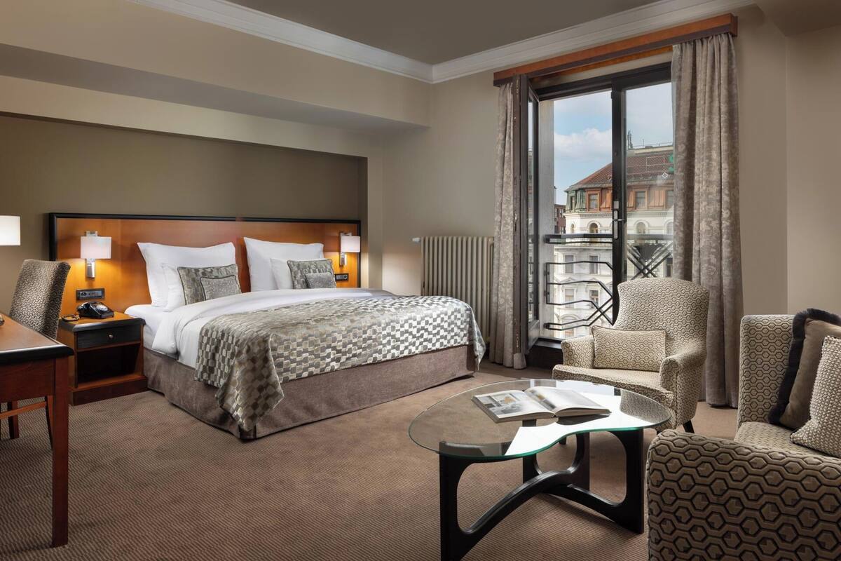 A hotel room with a bed, bedside table, lamp, chair, and a glass table with a magazine.